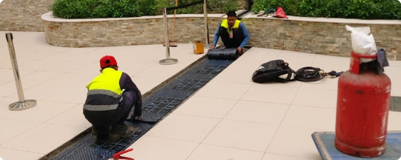Technicians applying waterproofing membrane to an exterior drainage trench